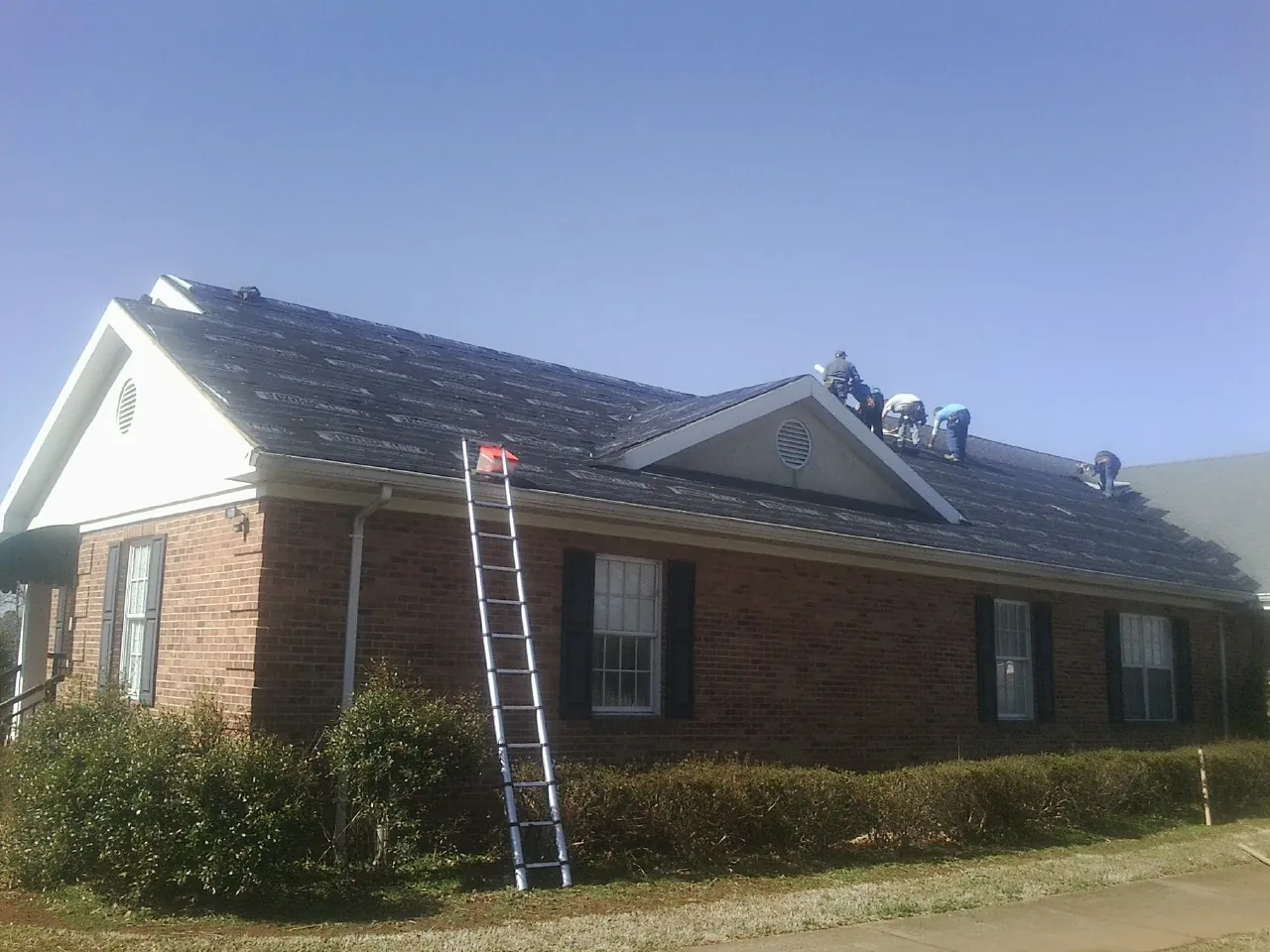 Crew tearing shingles off a brick ranch roof with a ladder set — Metal Roof Repair work by our crew in Tahlequah