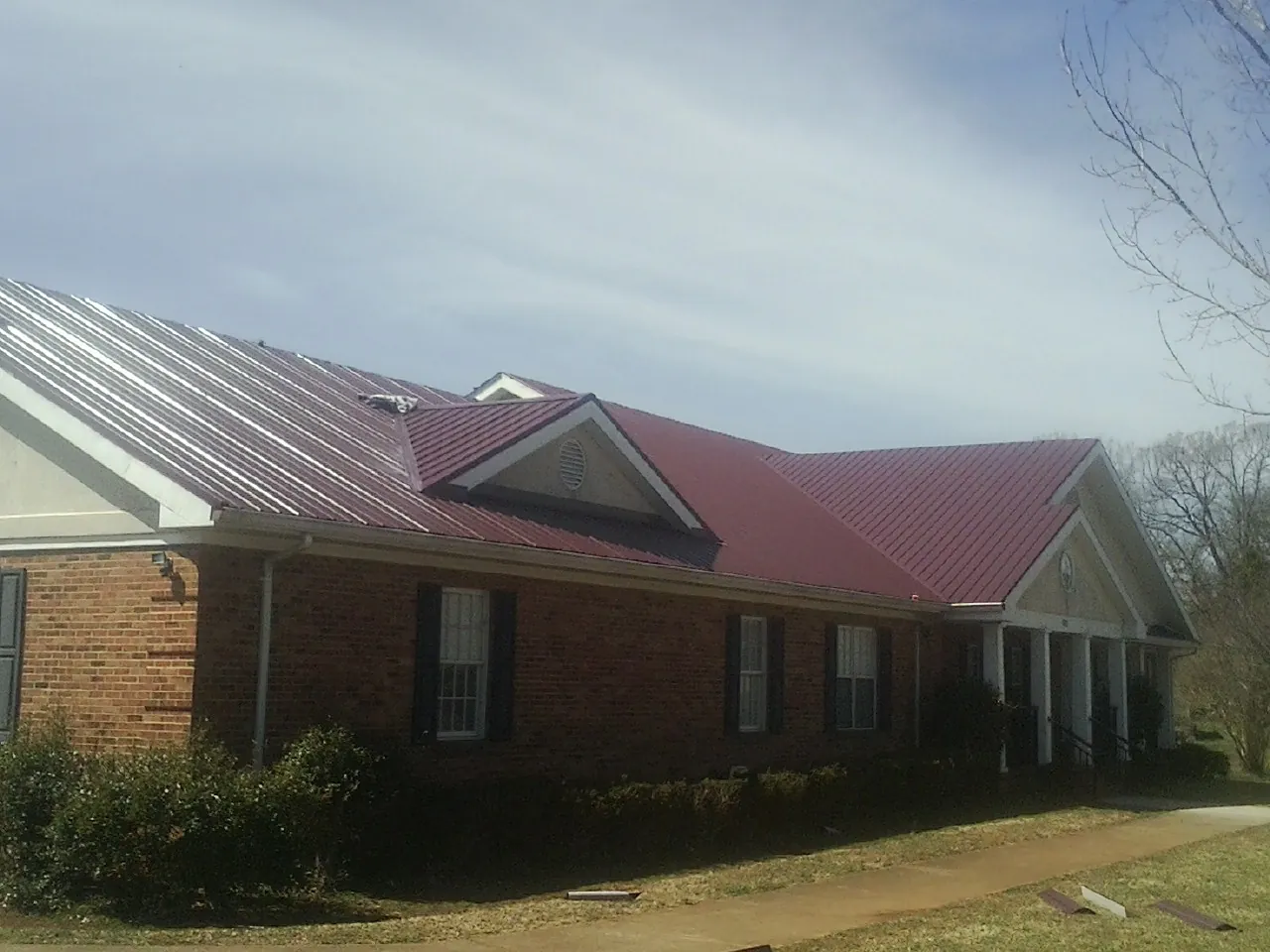 Red metal roof with gabled entries on a long brick building, from a Hail Damage Roof Repair job in Tahlequah
