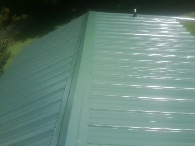 New green metal panels meeting at the ridge of a roof — Flat Roof Repair work by our crew in Tahlequah