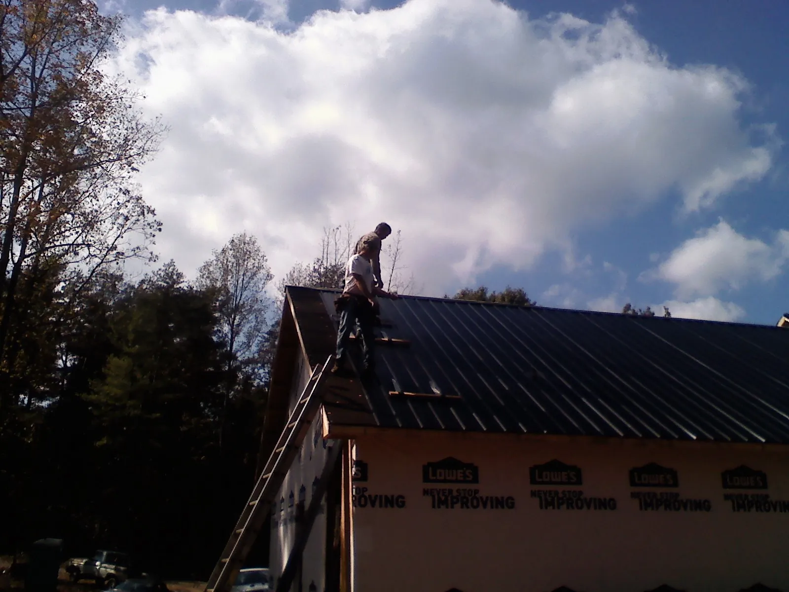 Roofer fastening dark metal panels high against a cloudy sky, from a Roof Inspection job in Tahlequah