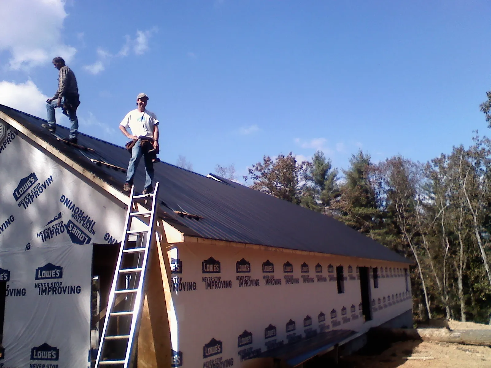 Two roofers standing on a long dark metal roof over a wrapped building in Tahlequah