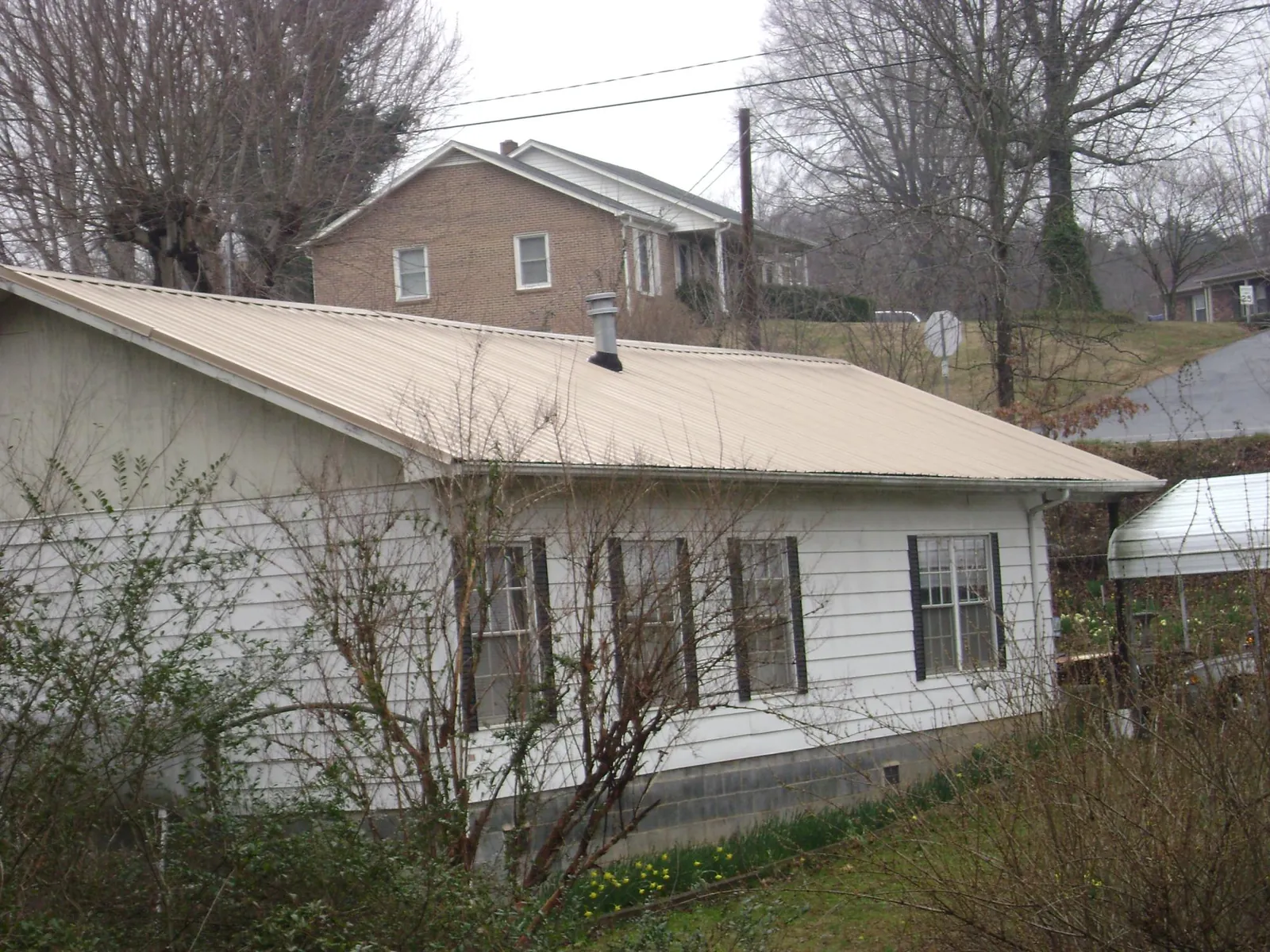 Tan metal roof on a white sided house set into a hillside — Commercial Roofing by Roofing Brothers in Tahlequah