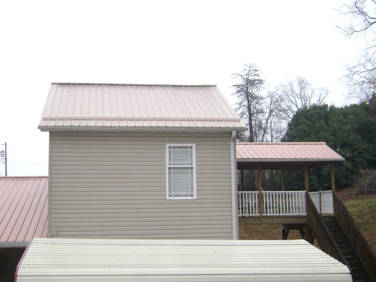 Tan metal roofs on a two story addition and attached porch, from a Roof Replacement job in Tahlequah