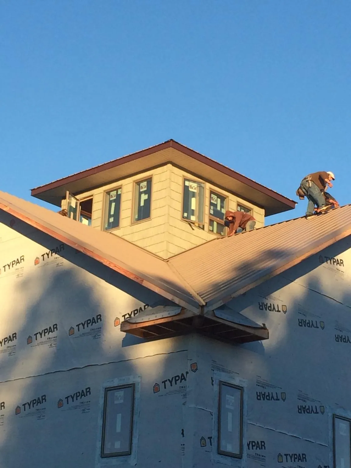 Roofers working around a rooftop cupola on a new metal roof at sunset — Roof Waterproofing in Tahlequah by Roofing Brothers